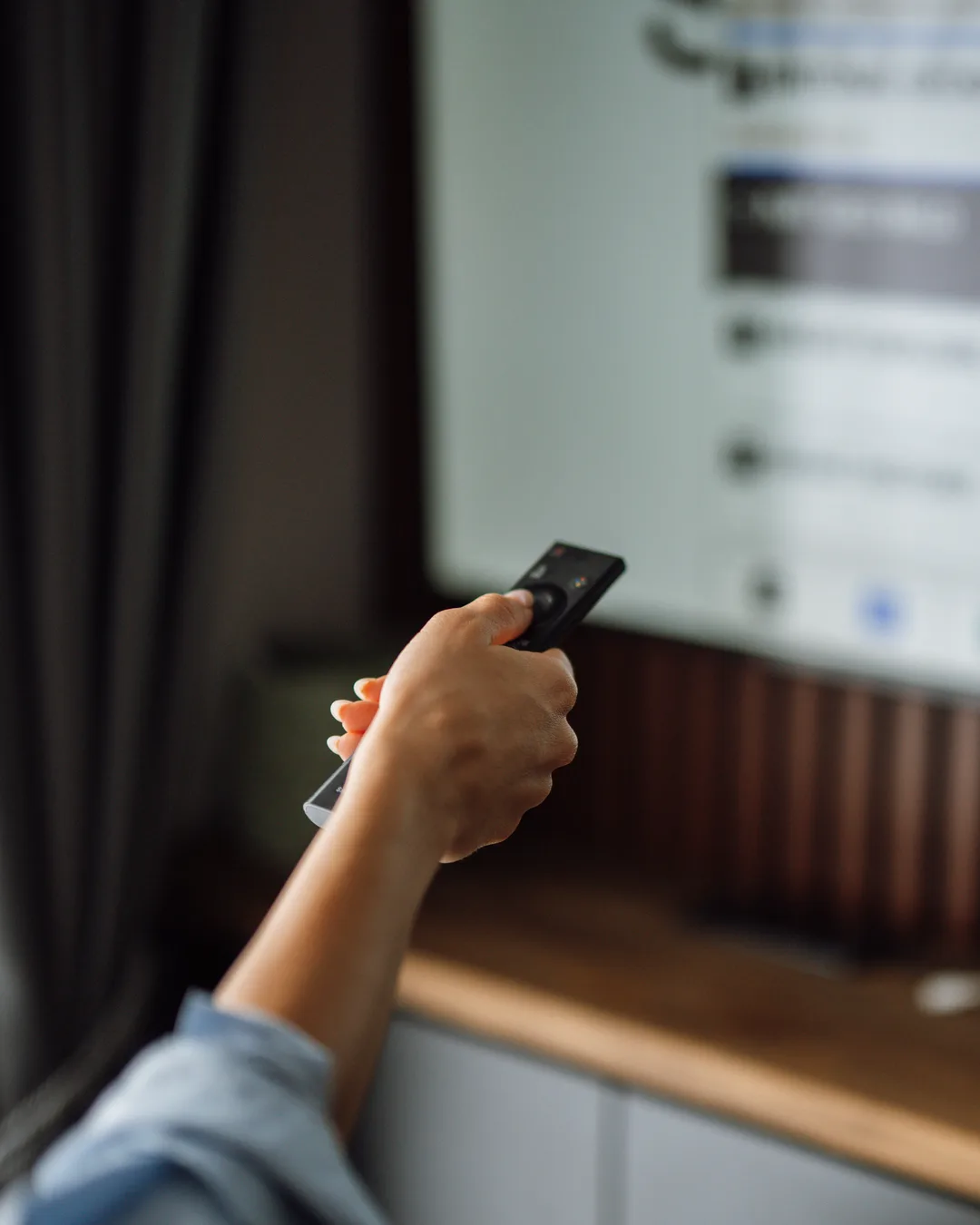 Mano con un mando a distancia apuntando a un televisor que muestra un menú, sobre un mueble de madera en un salón